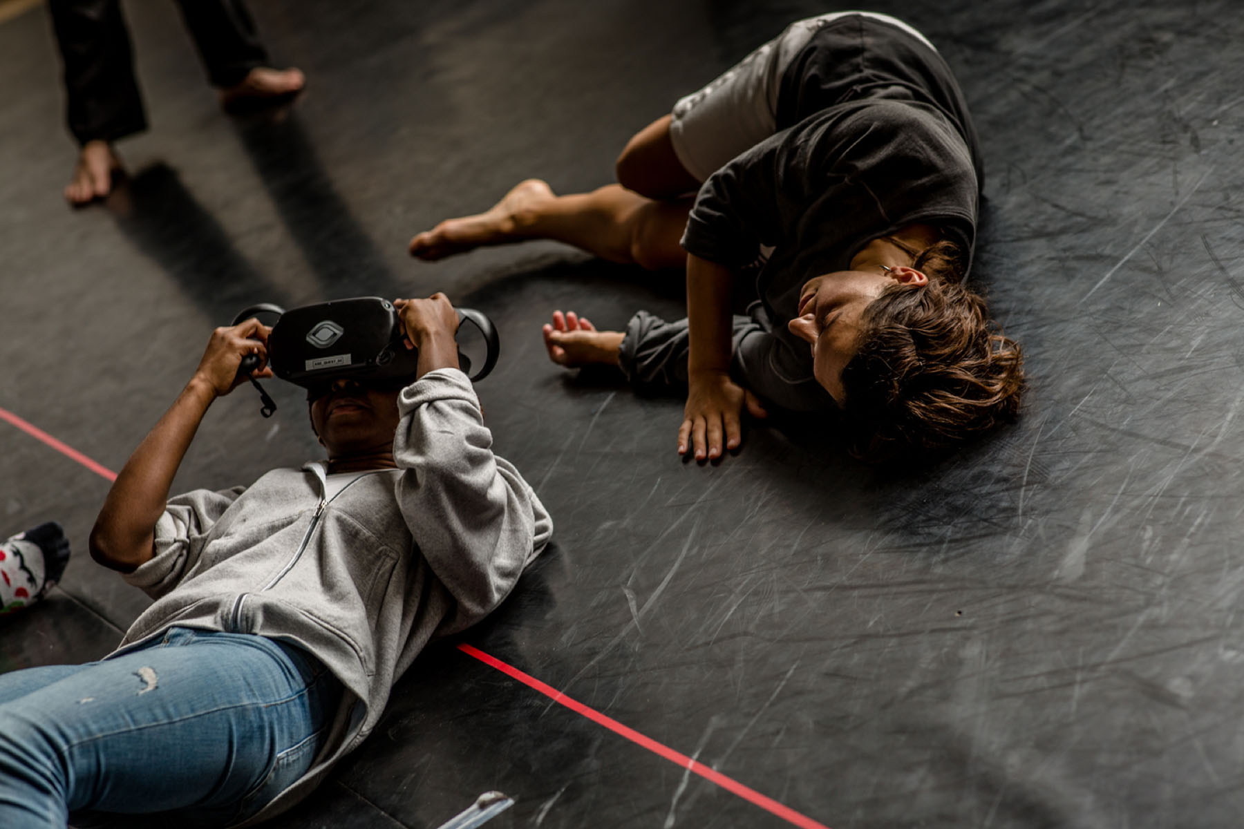 A dancer and a person lying on the floor one is wearing a VR headset